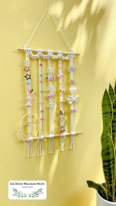 a wall hanging made out of macrame beads and other beaded items with a plant in the foreground