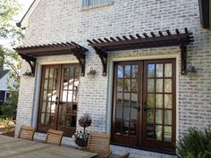 an outdoor dining area with wooden table and chairs next to a brick building that has french doors