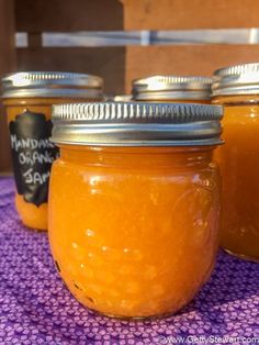 three jars filled with orange marmalade sit on a purple table cloth next to each other