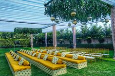 an outdoor ceremony setup with yellow couches and gold pillows on the back row, surrounded by greenery