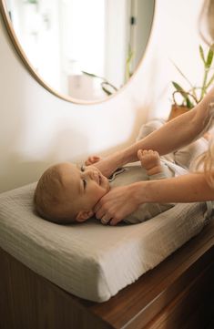 a woman is holding a baby's hand over the top of a bed in front of a mirror