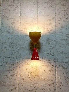 a red and yellow wall light sitting on the side of a white tiled wall next to a window