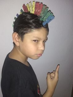 a young boy with colorful hair clips on his head pointing at the camera while wearing a black t - shirt