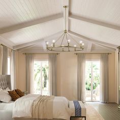 a bedroom with a bed, chandelier and two windows