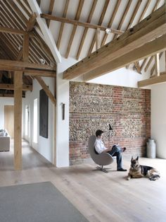 a man sitting in a chair next to a dog laying on the floor near a brick wall