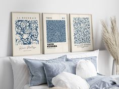 three blue and white prints on the wall above a bed in a room with pillows