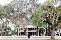 an old house with trees in front of it and a white picket fence around it