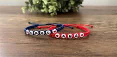 two red, white and blue bracelets sitting on top of a wooden table next to a plant