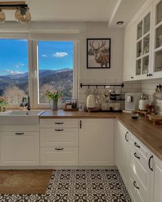 a kitchen with white cabinets and wooden counter tops next to a large window overlooking the mountains