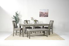 a dining room table with chairs and a bench in front of the white wall that has a painting on it