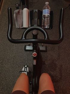 the legs of a person riding a stationary bike with water bottles and other items on it