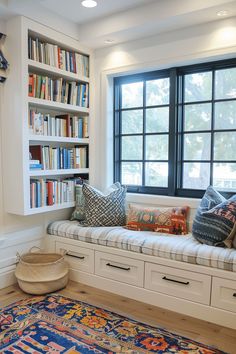 a window seat with bookshelves and pillows on it in front of a large rug