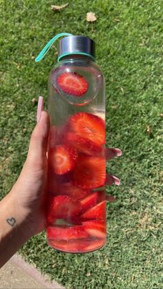 a person holding a water bottle with strawberries in it on the grass and one hand