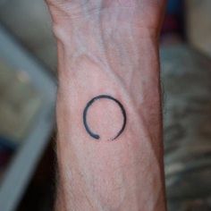 a man's wrist with a small black circle tattoo on the left side of his arm