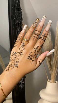 a woman's hand with hennap and tattoos on her left arm, holding a white manicure