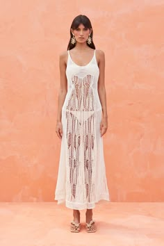 a woman standing in front of a pink wall wearing a white crochet dress