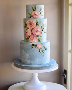 a three tiered blue cake with pink flowers on it sitting on top of a table