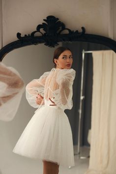 a woman standing in front of a mirror wearing a white dress