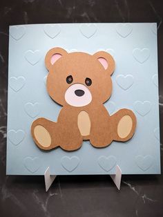 a brown teddy bear sitting on top of a blue card with hearts in the background