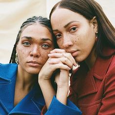 two women sitting next to each other with their hands on their face and looking at the camera