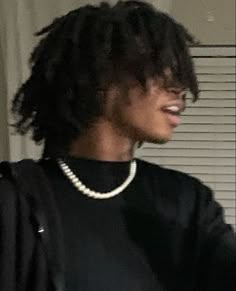 a young man with curly hair wearing a black shirt and pearls on his necklace is looking into the mirror