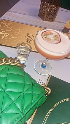 a green purse sitting on top of a table next to a glass filled with liquid