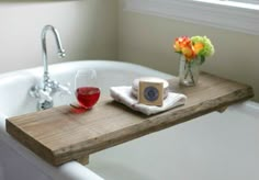 a bath tub with a wooden tray holding soap and a glass of wine