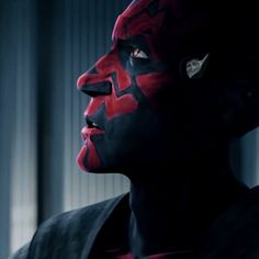 a man with red and black face paint looks off to the side in a dark room