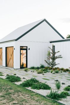 a white building with two doors and windows on the side of it, surrounded by green grass