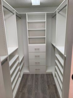 an empty walk in closet with white shelving and drawers on the wall, along with wood flooring