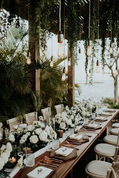 a long table with white flowers and greenery is set up for an outdoor dinner