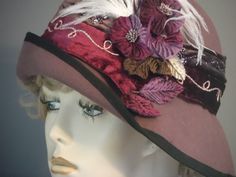 "This luscious mauve felt has been hand made using a vintage hat block. All hand made. Added flowers, feathers and 2 tone velvet band make this hat quite a statement piece. The 2.5\" band that encircles the crown is decorated with gold & lurex swirled trim, & sequins, against mauve and burgundy velvet. White small ostrich feathers, and light and dark purple flowers with wine, purple and green velvet leaves adorn the side in a lush melange. Black grosgrain ribbon trims the edge of brim. A special Handmade Fitted Vintage Fascinator, Handmade Formal Hats, Elegant Red Felt Hat For Formal Occasions, Elegant Fitted Brown Felt Hat, Elegant Fall Cloche Hat, Elegant Wide Brim Costume Hat For Winter, Handmade Fitted Hats For Formal Occasions, Handmade Fitted Formal Hats, Elegant Brown Top Hat For Winter