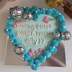 a heart shaped cake with blue icing and silver decorations on the top that says dancing queen young & sweet only 17