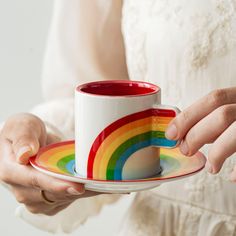 a woman holding a coffee cup and saucer with a rainbow design on the rim