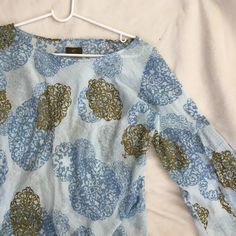 a blue and gold patterned top hanging on a white hanger next to a bed