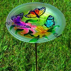 a glass plate with butterflies painted on it sitting in the grass next to a stick