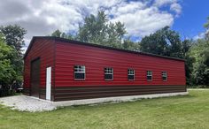 a red and brown building sitting on top of a lush green field next to trees