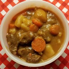 a white bowl filled with stew and carrots on top of a checkered table cloth