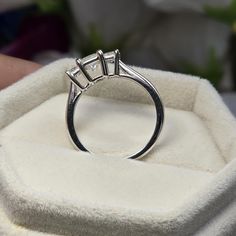 a three stone diamond ring sitting on top of a white velvet box with flowers in the background