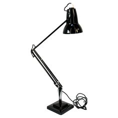 a black desk lamp on a white background with the cord plugged in to it