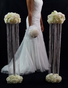 a woman in a wedding dress is standing next to flowers and beads on poles that are hanging from the ceiling