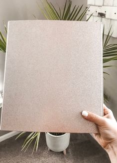 a person holding up a square tile in front of a potted plant