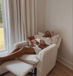 a man laying on top of a white chair next to a window