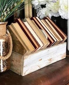 a wooden box filled with books sitting on top of a table next to a vase