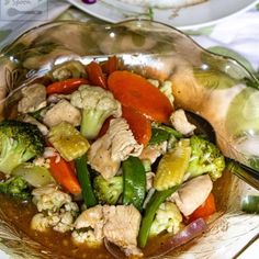 a glass bowl filled with meat and vegetables on top of a table next to a plate of food