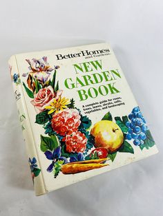 the new garden book is sitting on a white tablecloth with flowers and fruit in it