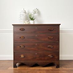 a wooden dresser sitting on top of a hard wood floor next to a white vase