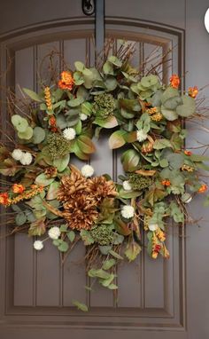 a wreath on the front door with flowers and leaves hanging from it's side