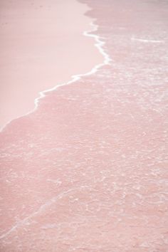 a person walking on the beach with a surfboard in their hand and one foot in the water