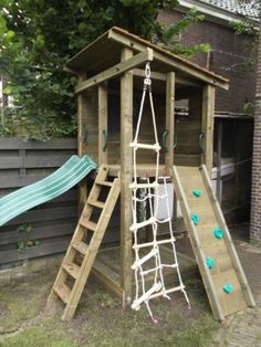 a wooden play structure with a slide and climbing frame in the back yard, next to a tree house